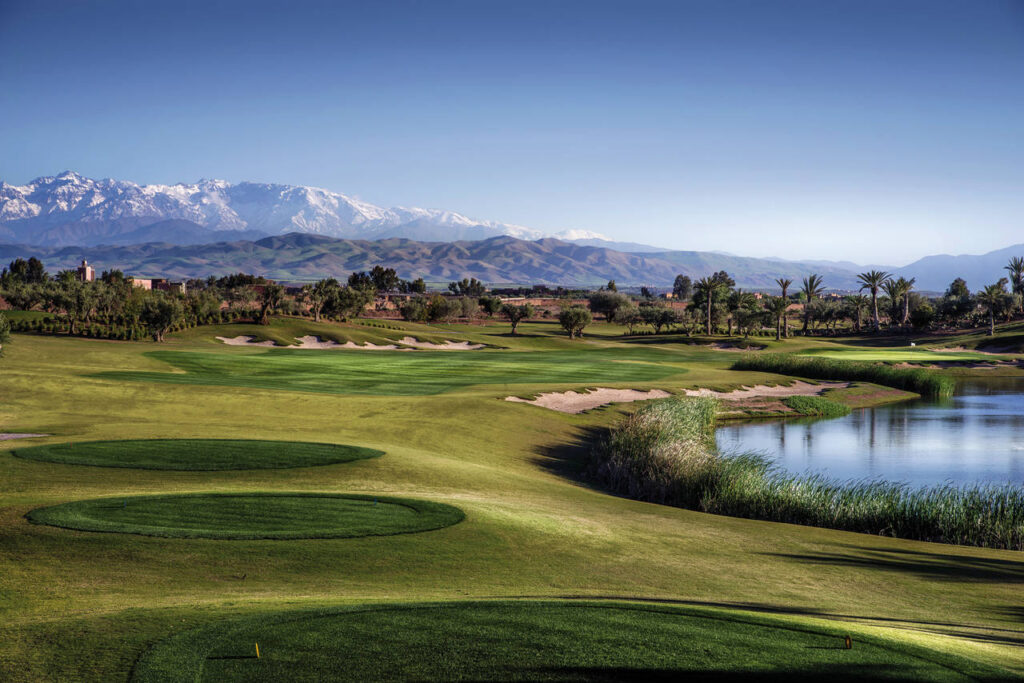 Lush golf course in Morocco with the Atlas Mountains in the backdrop under clear blue skies.
