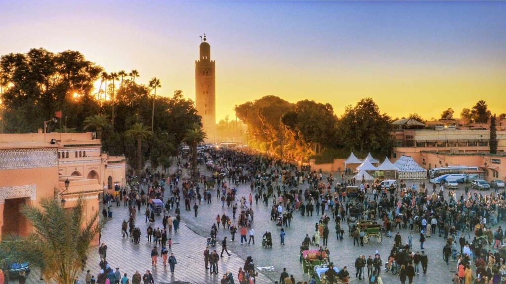Sunset over Jemaa el-Fnaa square in Marrakech with crowds and the Koutoubia Mosque silhouette in the background.