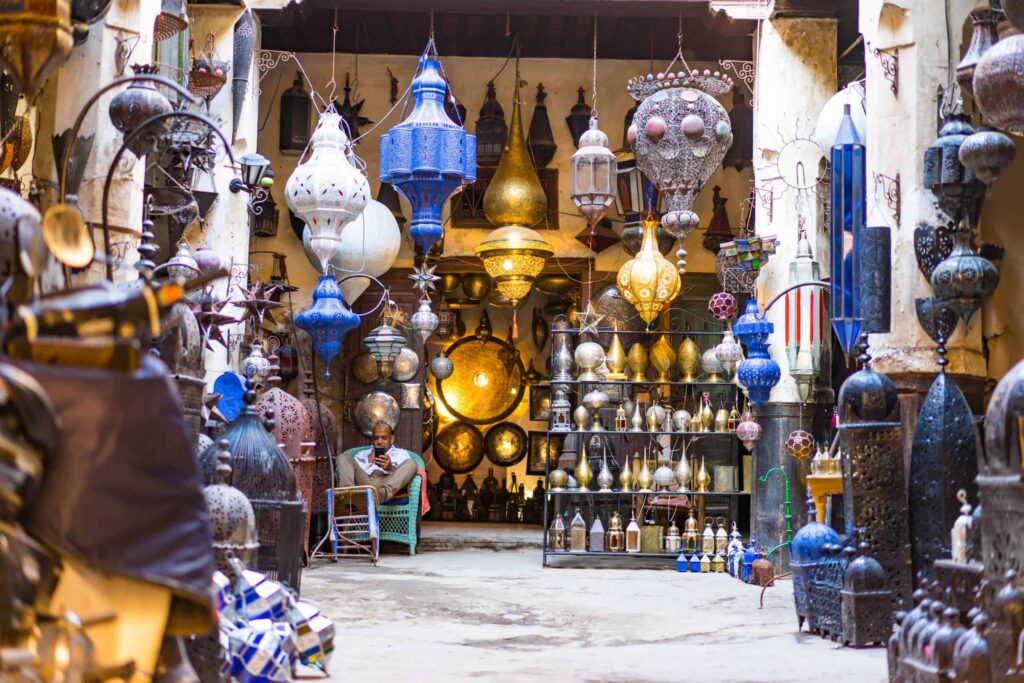 Colorful traditional Moroccan lanterns displayed in a bustling market with a shopkeeper in the background.