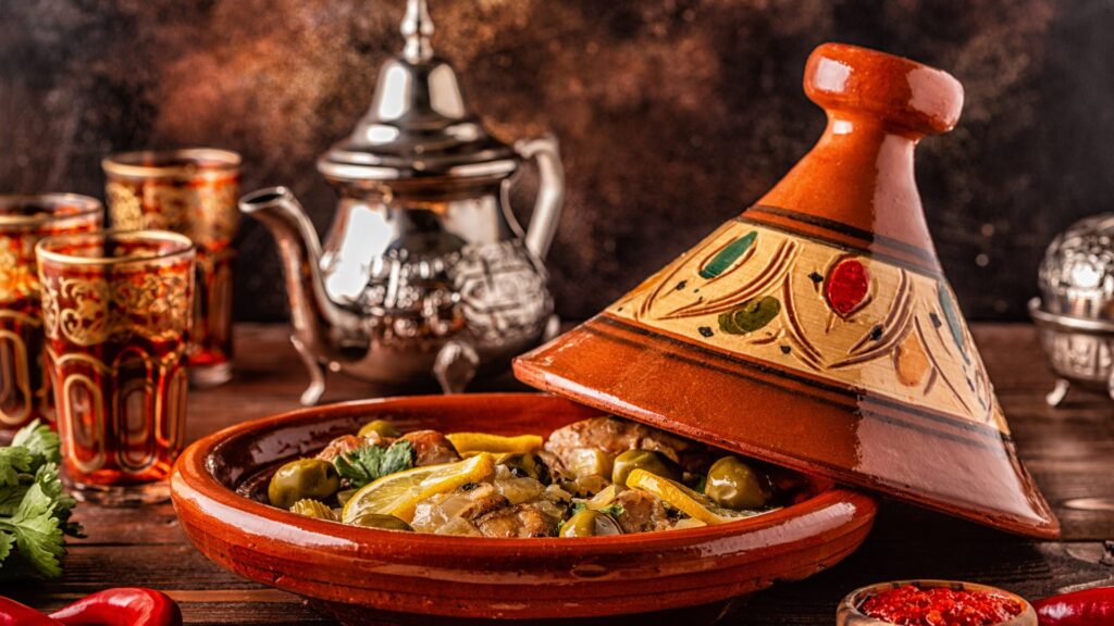 Traditional Moroccan tagine dish served with colorful tea glasses and silver teapot on a wooden table.