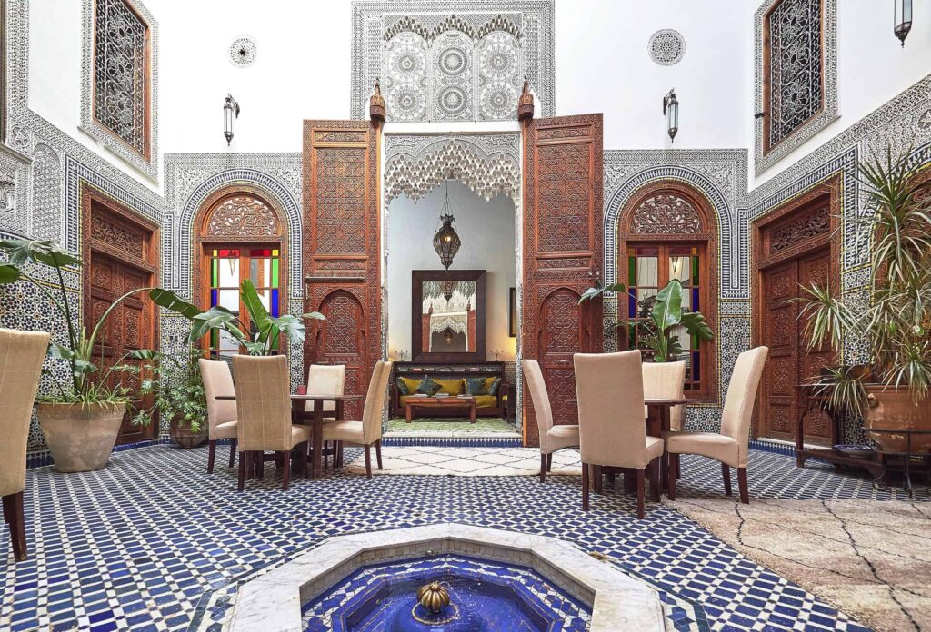 Elegant courtyard of a traditional Fes Riad with intricate Moroccan tile work and ornate wood carvings.