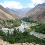 Meandering river in Ourika Valley with lush greenery and towering Atlas Mountains.