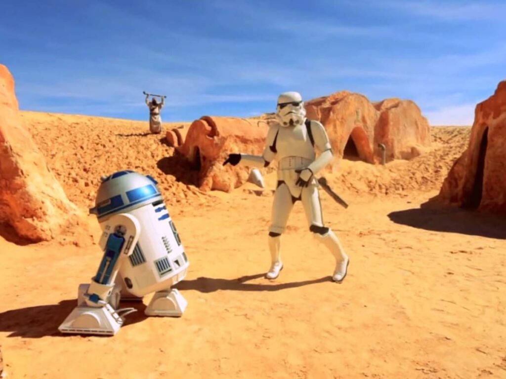 Iconic Star Wars characters R2-D2 and a Stormtrooper on the set in the Sahara Desert, representing the planet Tatooine in the film series.