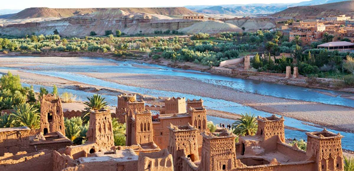 Scenic view of the Kasbah of Aït Benhaddou with river and mountains in the background.