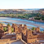 Scenic view of the Kasbah of Aït Benhaddou with river and mountains in the background.