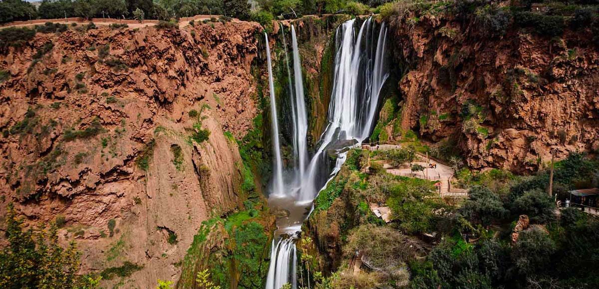 Scenic view of Ouzoud Waterfalls with lush greenery and red cliffs